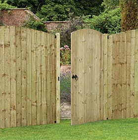 Natural wood fence gate with an arched top and black metal hinges, set in a grassy landscape.